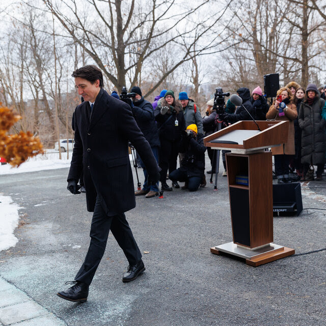 A man in dark coat and tie walks away from a lectern after facing a crowd of reporters.