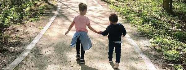 Two children hold hands as they walk down a dirt path in spring. 