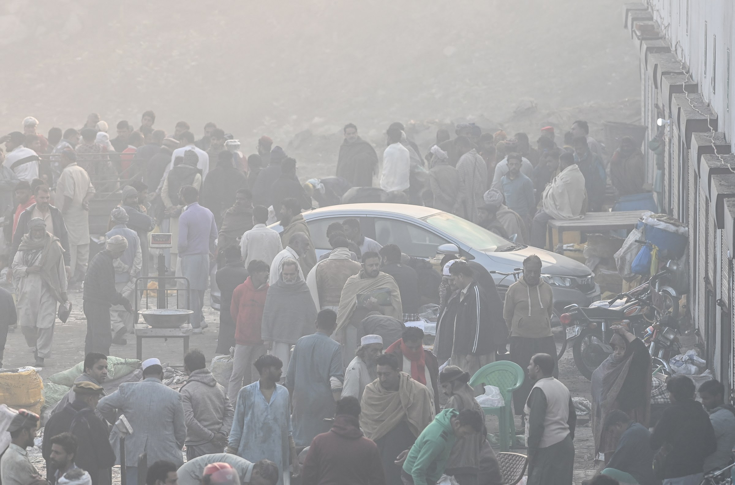 People standing around a parked car on a very smoggy day.