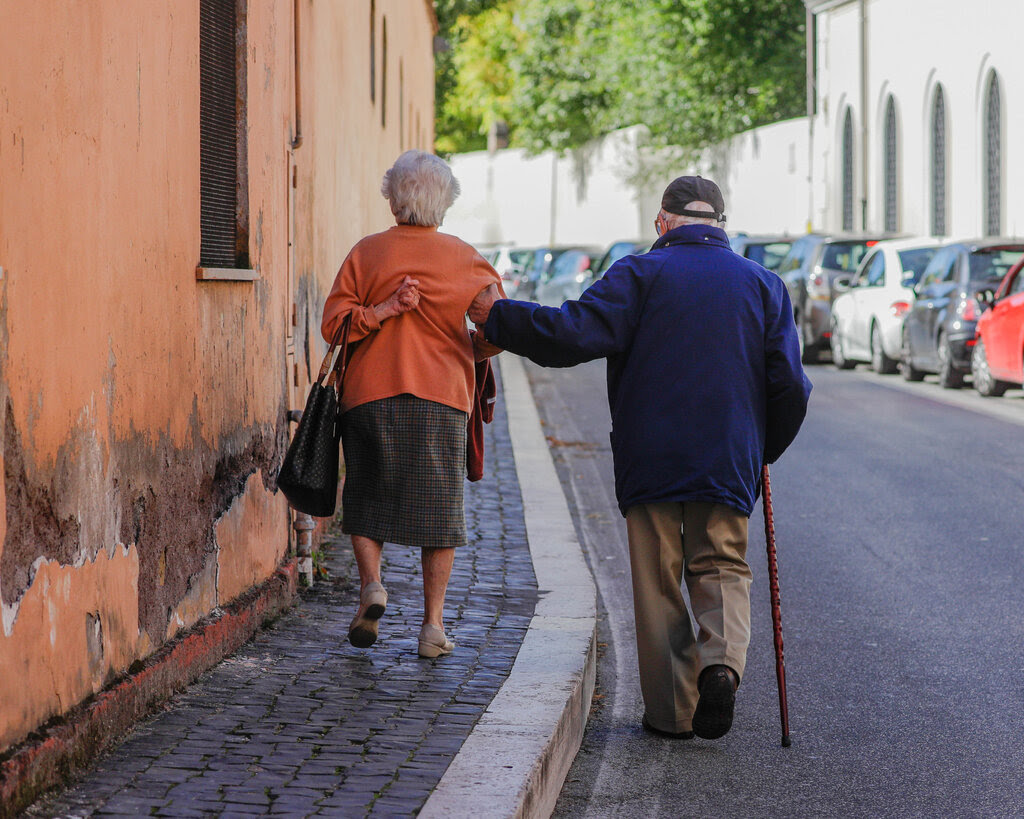 An elderly couple walking along a street in Rome.