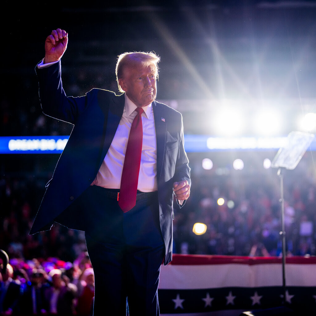 Donald Trump walks out onto a stage with an arm lifted in the air. 