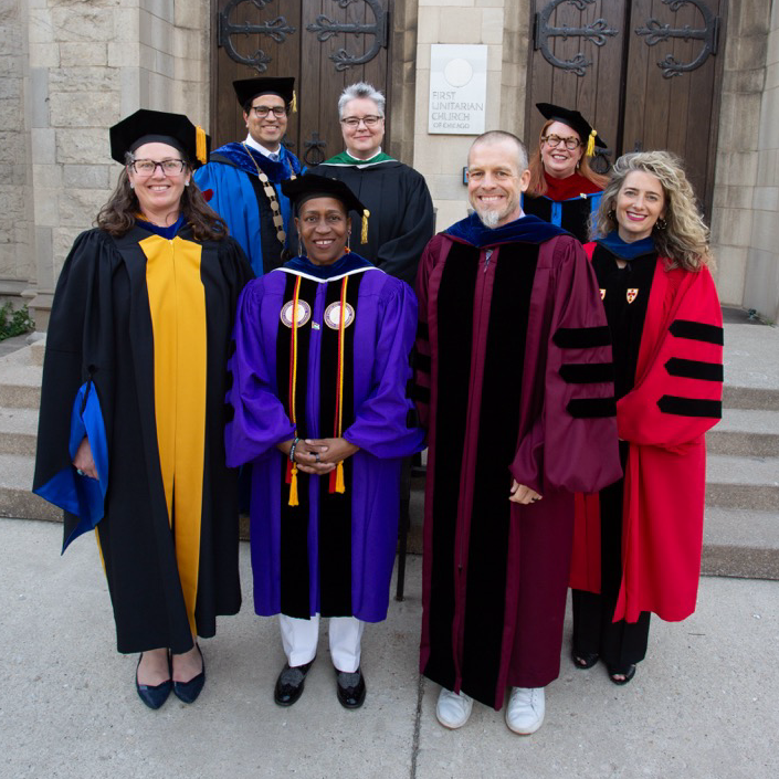 Graduates stand outside in regalia