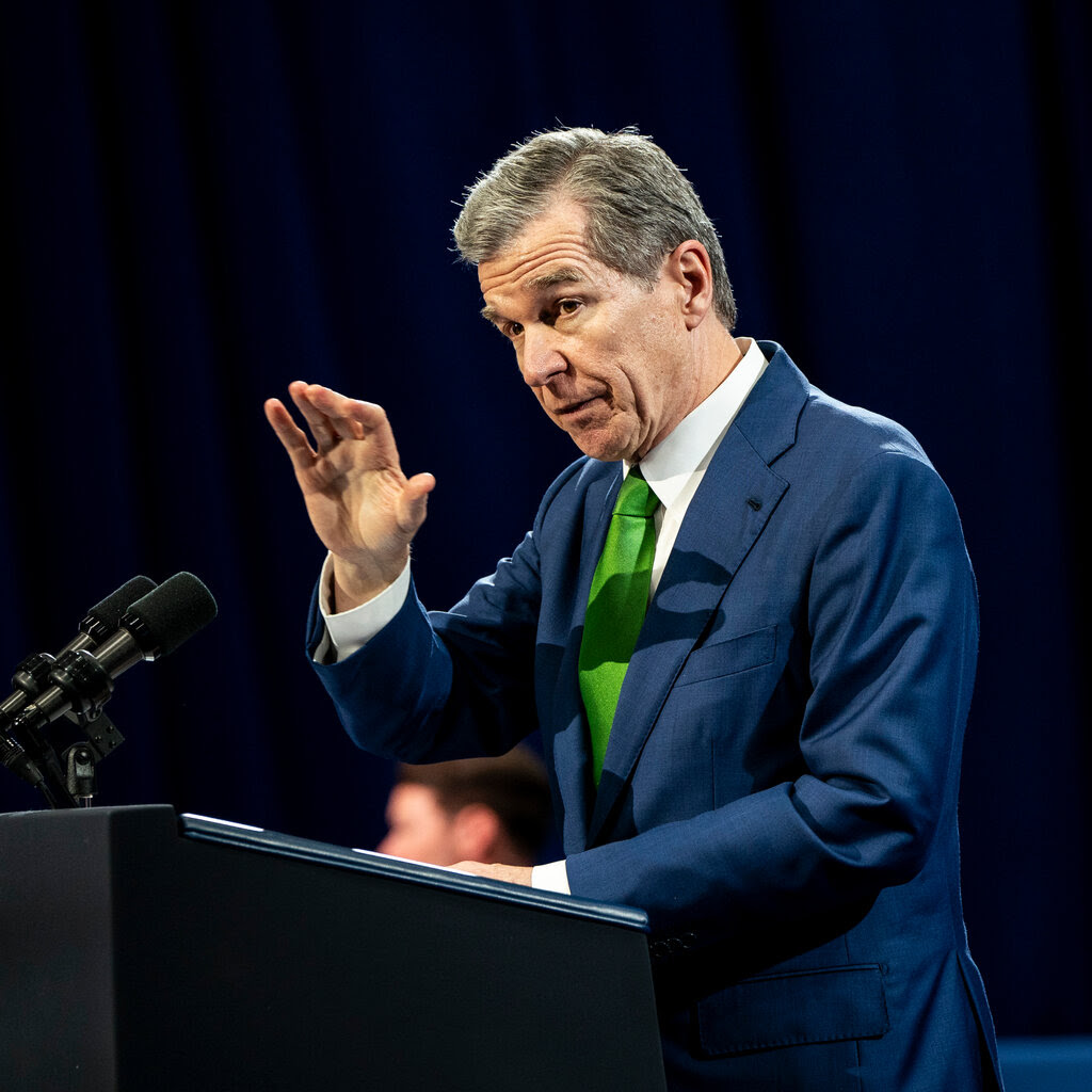 Roy Cooper giving a speech at a lectern and gesturing with his right hand.