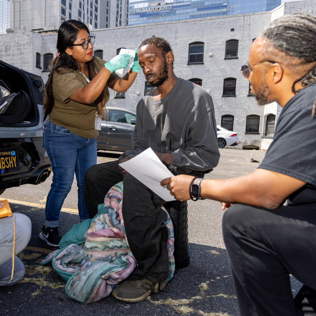 Two people tends to a homeless man wearing a gray sweater.