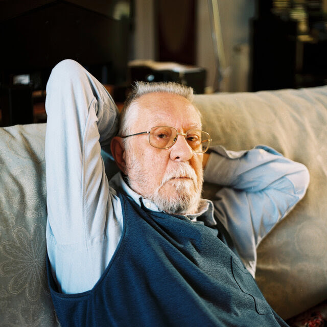 A portrait of Nazario Luque Vera, informally sitting on a sofa, his hands behind his head. 