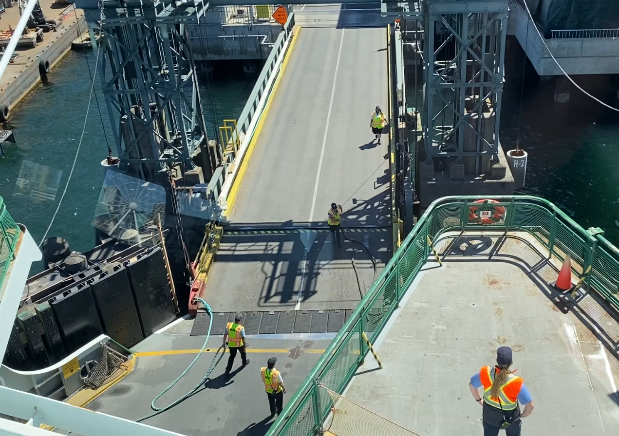 Five people in safety vests working on a ferry and a terminal transfer span to prepare for departure