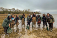 Ten people pose in a semi-circle in an estuary at the Pine Knoll Shores Aquarium on an overcast day