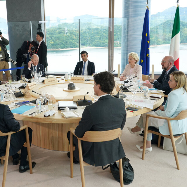 A group of leaders seated around a table, with a view of water and green hills outside the window.