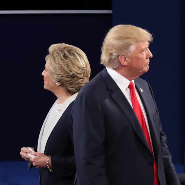 Facing away from each other, Hillary Rodham Clinton stands onstage on the left and Donald Trump stands on the right.