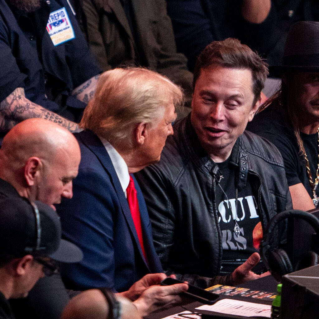 Donald Trump, in a suit, sits with Elon Musk, who is wearing in a leather jacket. 