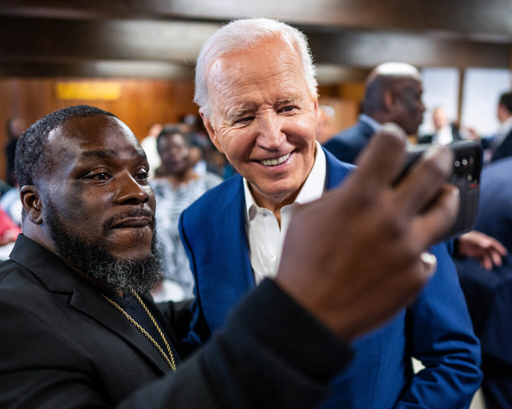 A man holds up a phone for a selfie with President Biden. 