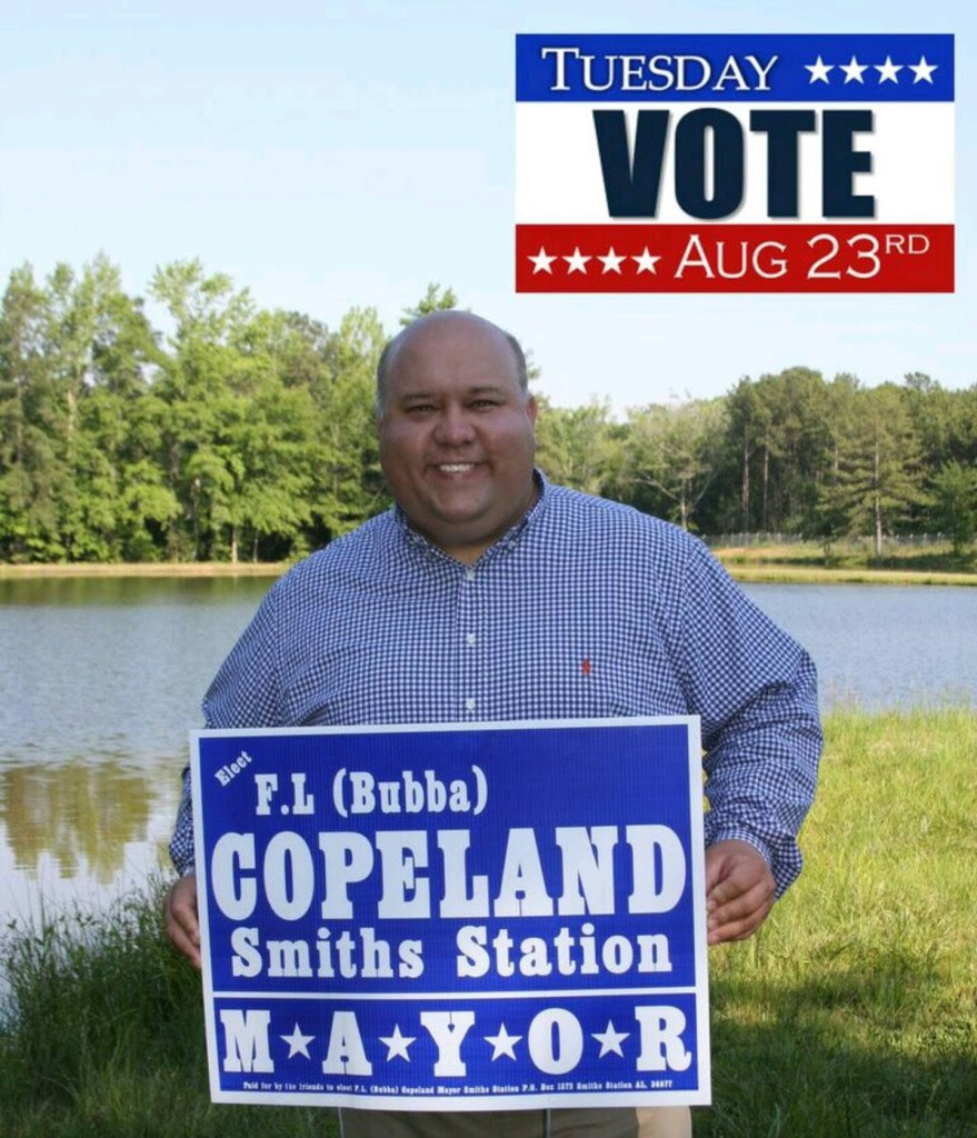 A photo of Smiths Station mayor and local preacher F.L. "Bubba" Copeland holding a campaign sign, with a reminder to vote in the top right corner.