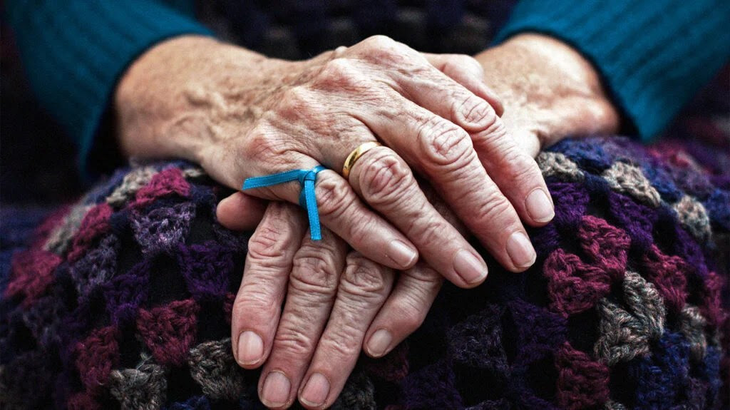 The hands of an older adult with a blue ribbon tied around one finger