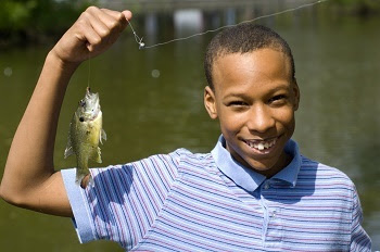 young boy smiling and holding up a fish on a line
