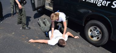 a forest ranger recruit patting down a volunteeras part of a crime prevetion exercise