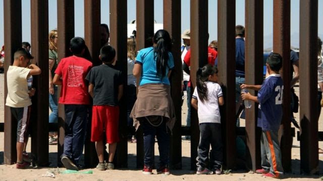 Crianças olham através do muro da fronteira EUA-México