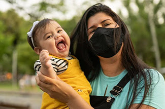 Woman in face mask holds smiling infant