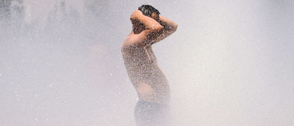 Shirtless man stands in water from sprinklers