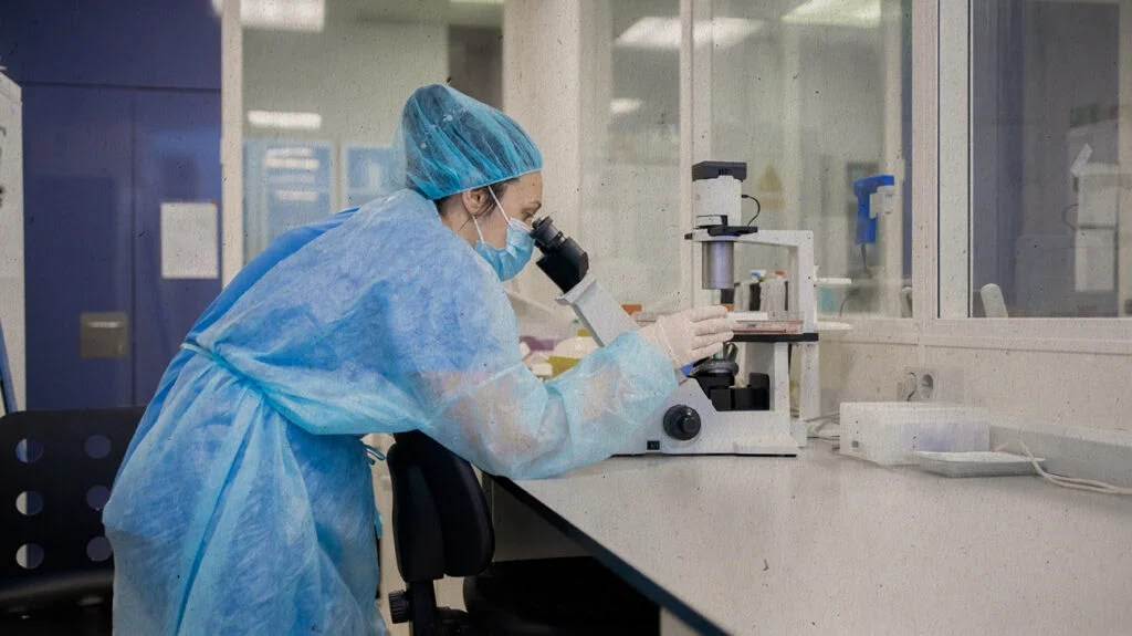 Scientist wearing protective clothing looks in a microscope