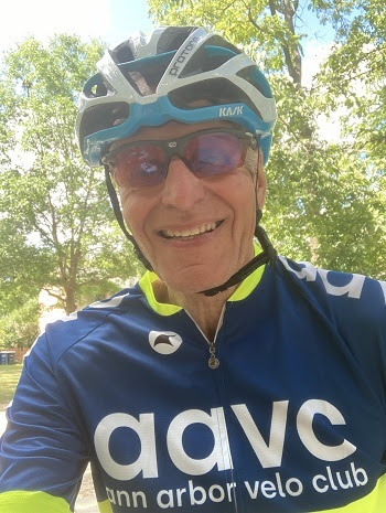 head and shoulders view of a smiling man wearing bike helmet, sunglasses and a dark blue and neon yellow shirt that says ann arbor velo club