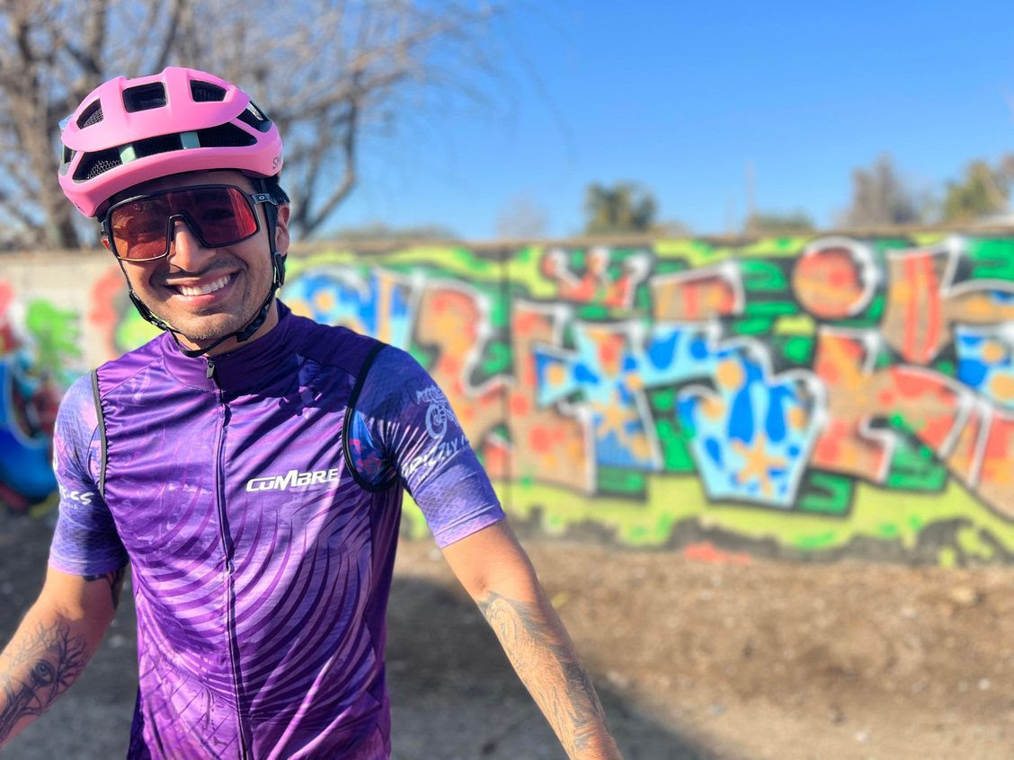 a man in a purple shirt and helmet standing in front of a graffiti wall
