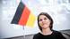 Annalena sorri timidamente. Ao fundo, uma bandeira da Alemanha.