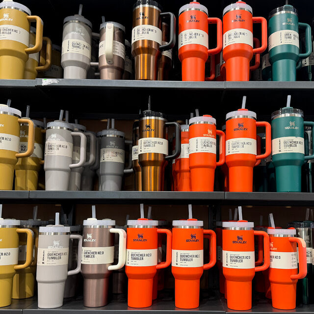 Three store shelves of Stanley tumblers in a variety of colors including yellow, gray, silver, orange and teal green.