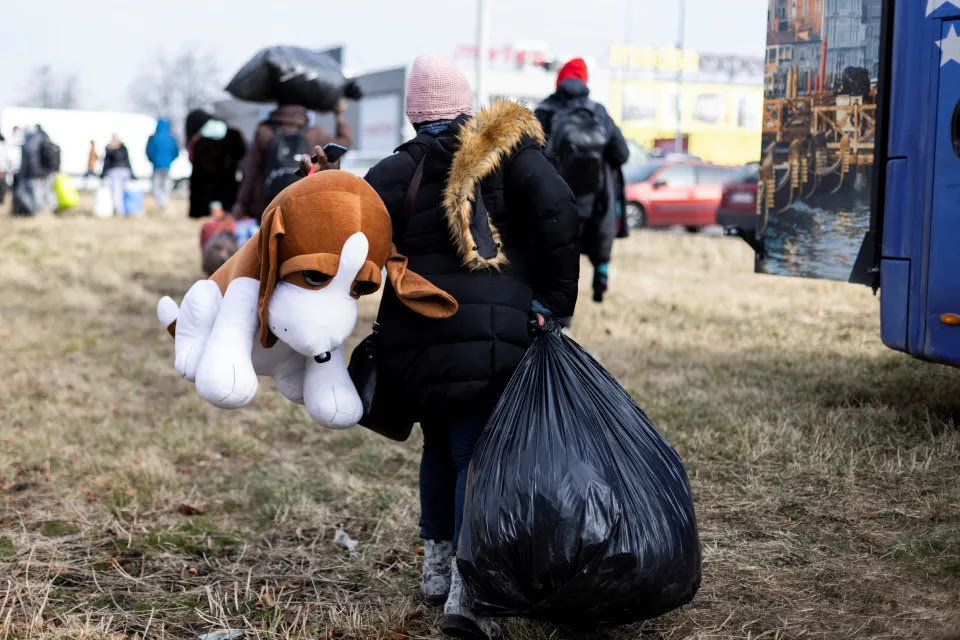 A Ukrainian refugee carries a large garbage bag and a large stuffed toy.