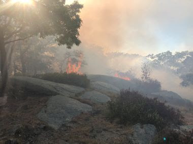 Smokey landscape with flames coming from the area beyond some rocks