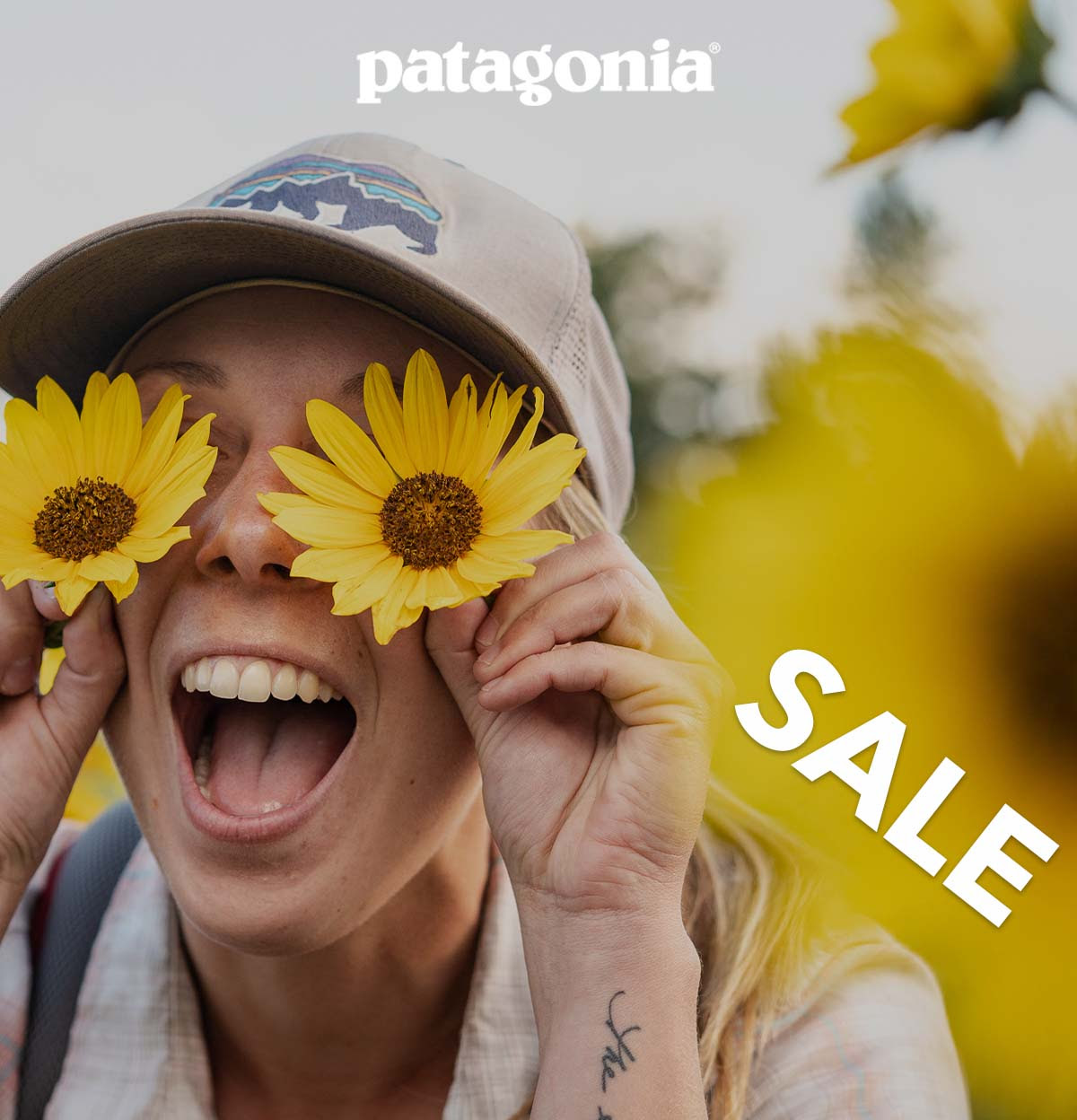 Sale. A person holds two yellow flowers over their eyes while smiling broadly.