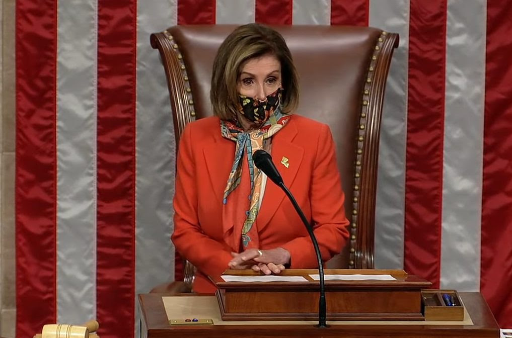 Nancy Pelosi stands behind a podium with an American flag behind her