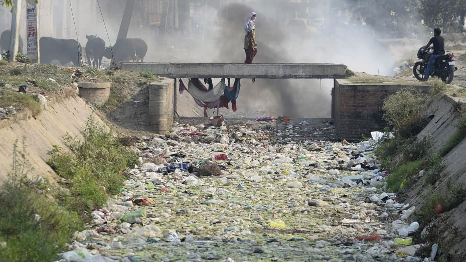An Indian woman crosses a bridge as workers burn plastic bags and garbage in dry canal in Jalandhar, India on May 10, 2018.