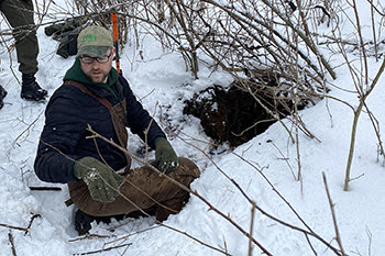 DNR biologist outside bear den in snowy forest