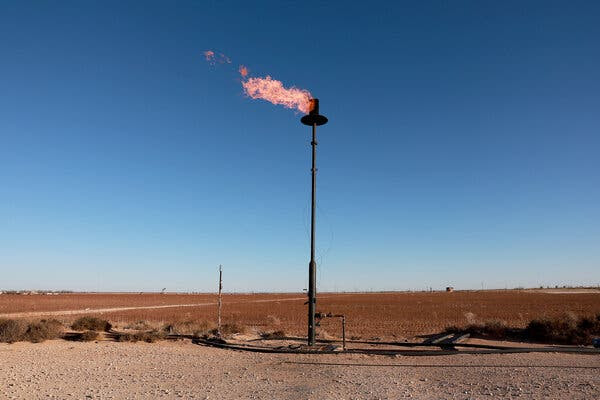 An orange flame shoots out to the
              left from the top of a tall vertical pipe that rises from
              a rust-colored desert landscape.