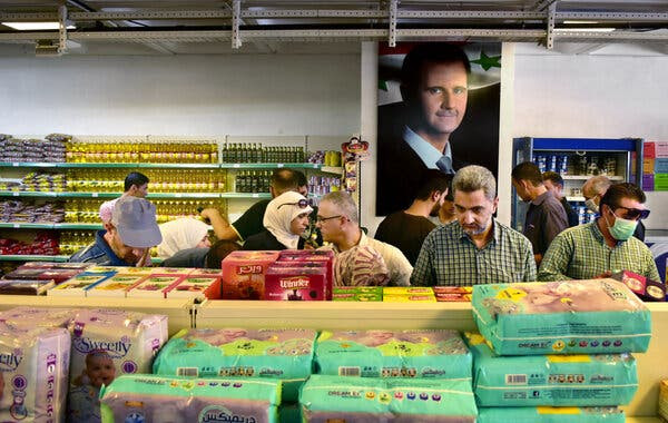 Buying food in Damascus with a photo of Syria’s president in the background. With the rising cost of food, 60 percent of Syrians are at risk of going hungry.