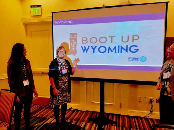 WDE staff look at Standards Supervisor Barb Marquer as she points to a screen she used for her presentation which features the logos for Boot Up Wyoming and the Wyoming Department of Education.