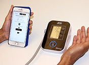 Close up of hands using blood pressure monitor next to a smartphone