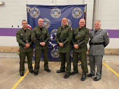 four ECOs and on State Police Officer pose for a picture with a back drop