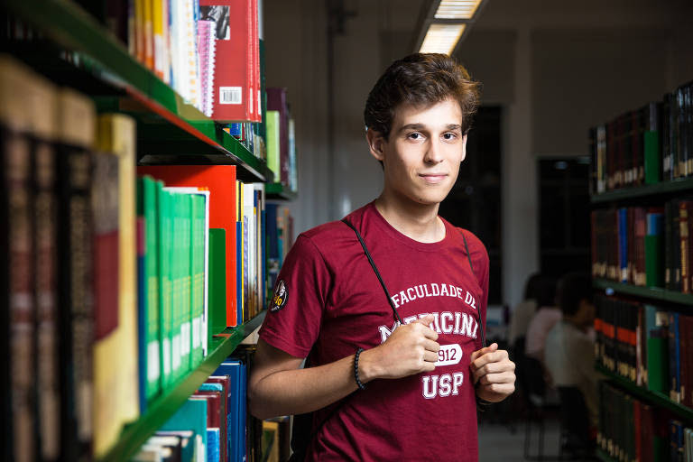 Jovem com camisa vinho ao lado de estante com livros