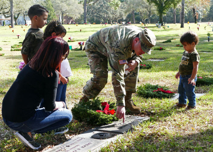 volunteers on wreaths across america day - family with small children placing a wreath and saying a veteran's name