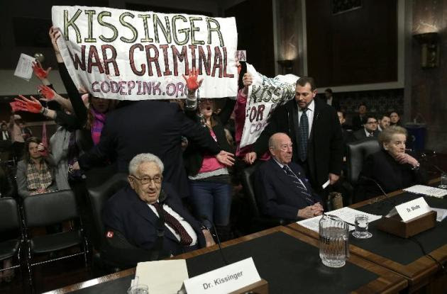 (De I a D) Los exsecretarios de Estado Henry Kissinger, George Shultz y Madeleine Albright sentados mientras manifestantes protestan contra el primero desplegando una pancarta que dice "Kissinger Criminal de Guerra", el 29 de enero de 2015, en el Senado estadounidense, en Washington, EEUU