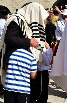 A father pulls his sons under
                  his tallit (prayer shawl) during the Priestly Blessing
                  at the Western Wall in Jerusalem. (Photo by Lilach
                  Daniel)