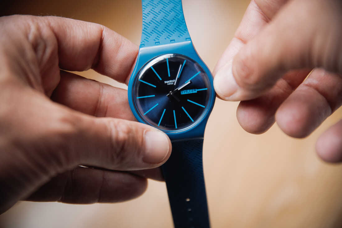 A person is turning the knob on the side of a blue watch to change the time.