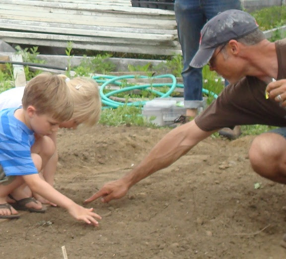 Charlie Rad helps a junior farmer plant
                        some seeds