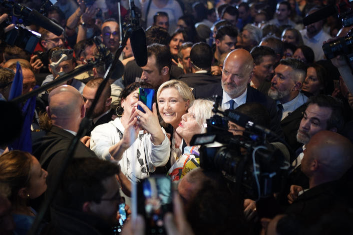 Marine Le Pen, with a beaming smile, poses for a selfie taken by one of her supporters, also of middle age and with bleached blond hair, at a campaign rally.