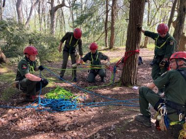 Rangers tying off different colored ropes to a tree in the woods during training