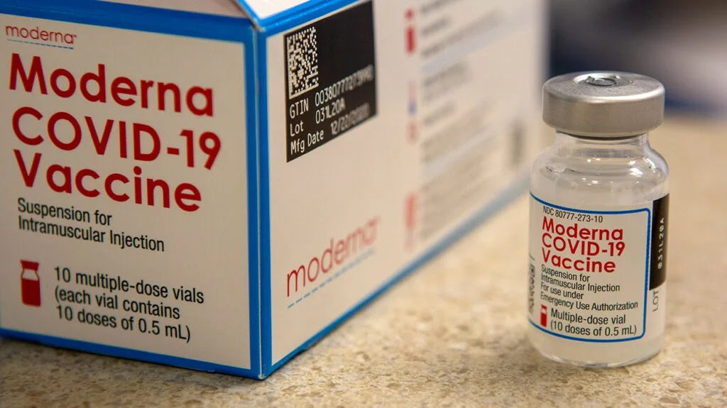 a glass bottle and box with the words 'moderna COVID-19 vaccine' are on a table