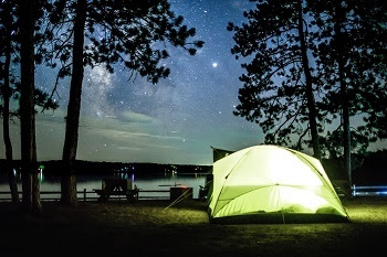 yellow tent, lit up from within, on the shores of Big Bear Lake, dark sky with hundreds of stars