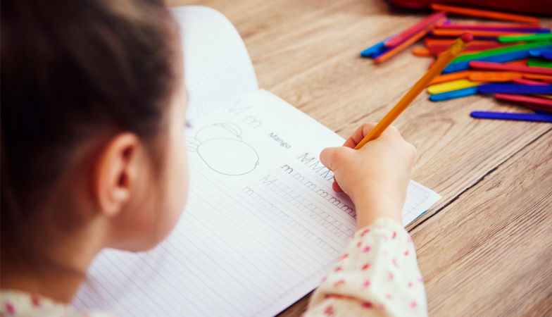 Foto de mão de uma criança escrevendo em caderno 