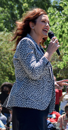 Governor Gretchen Whitmer with a microphone and speaking to a crowd outdoors
